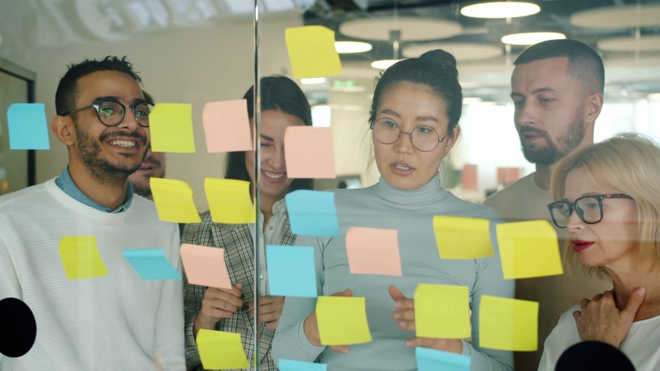 Colleagues looking at sticky notes on a glass wall while planning